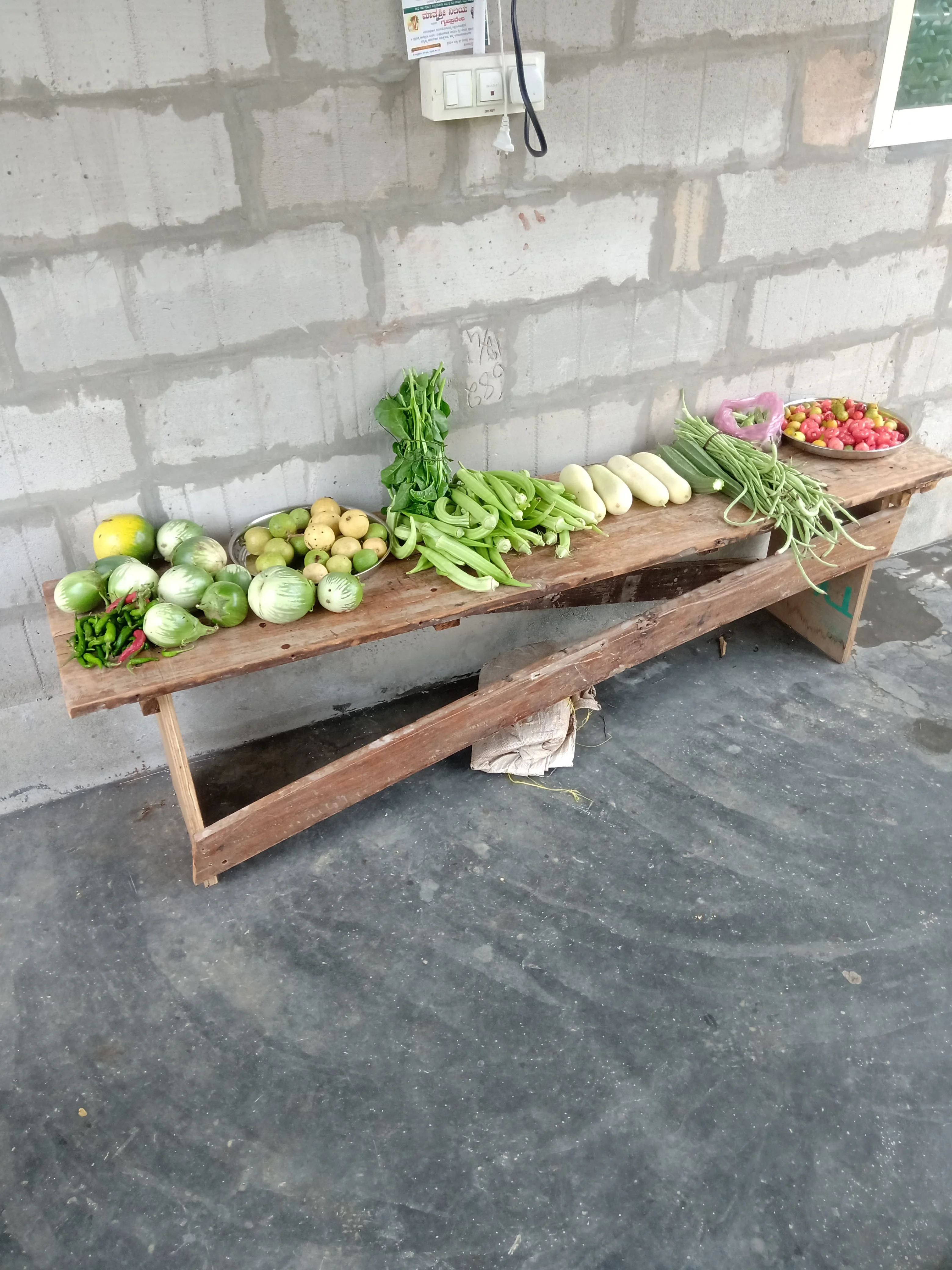 A wide shot of a wooden bench filled with a colorful assortment of freshly picked organic vegetables and fruits.